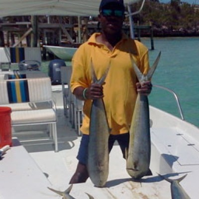 Person on a boat holding two large fish near clear water and dock.