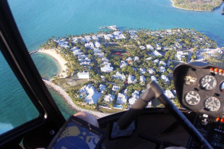 View of island with houses seen from helicopter cockpit above ocean.