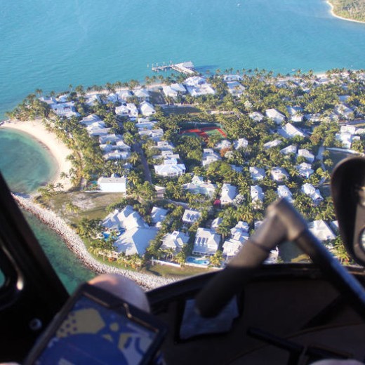 View of island with houses seen from helicopter cockpit above ocean.