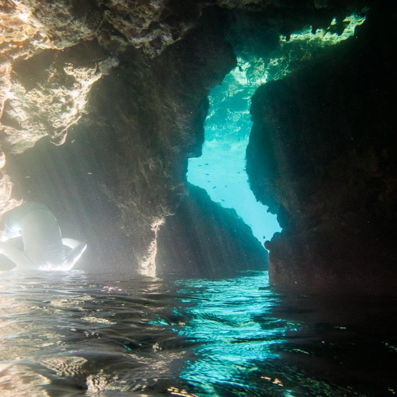 Sunlight beams into a rocky sea cave with clear turquoise water.