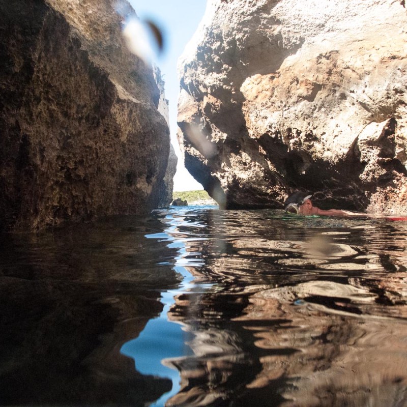 Narrow rocky canyon with water and a swimmer between rocks.