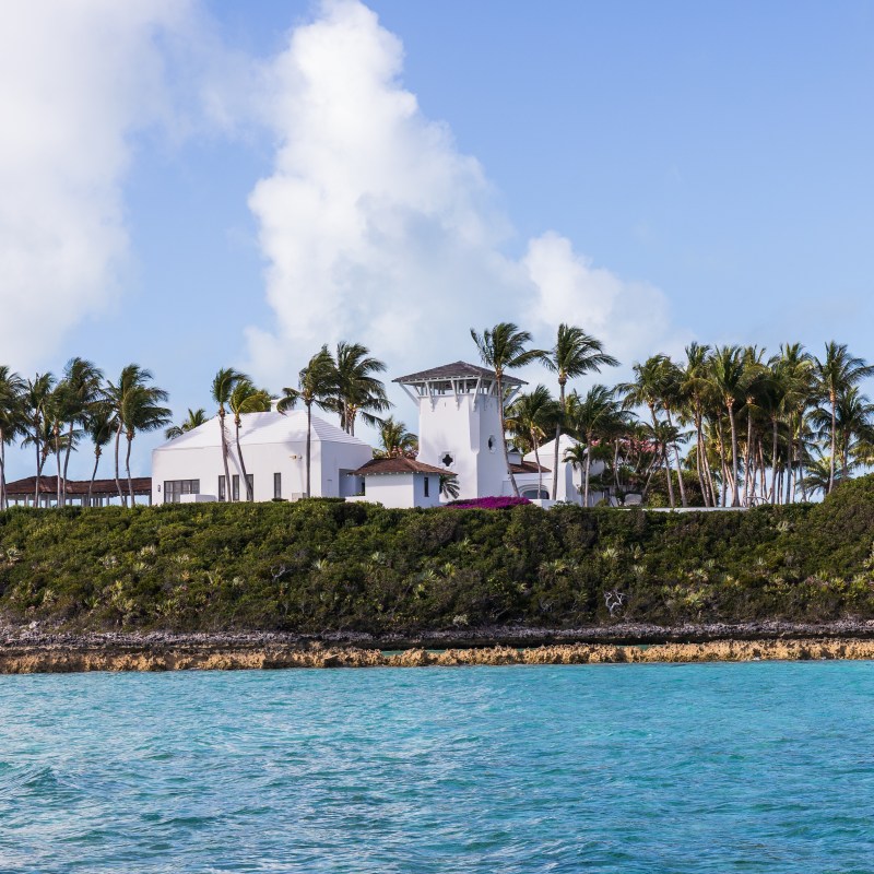 Beachfront white house with tower, palm trees, blue sky, and turquoise water.