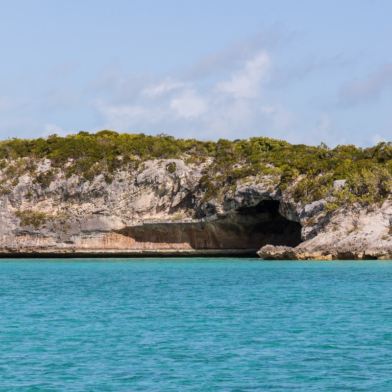 Rocky coastal cliffs with cave, turquoise water below.