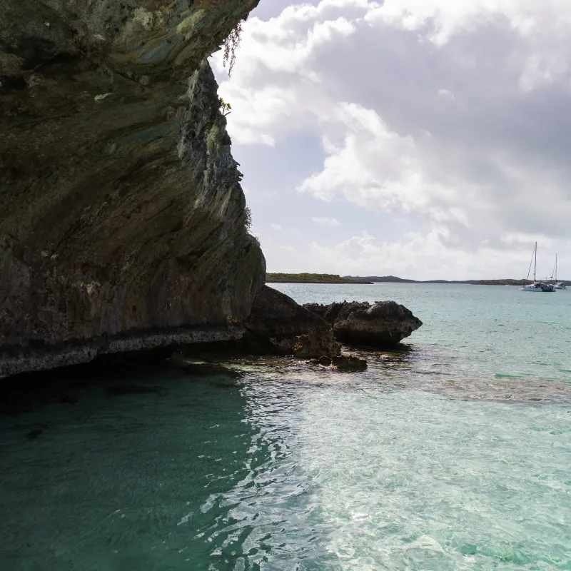 Rock formation over turquoise water with sailboats in distance.