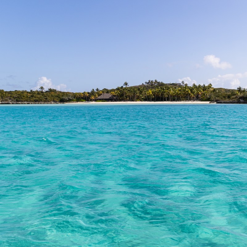 Tropical beach with turquoise water and a distant shoreline with palm trees.