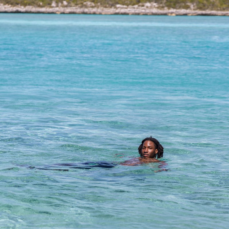 Person swimming in a clear blue ocean near a rocky shore.