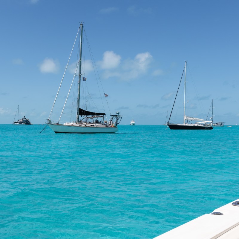 Sailboats anchored on clear turquoise sea under blue sky.