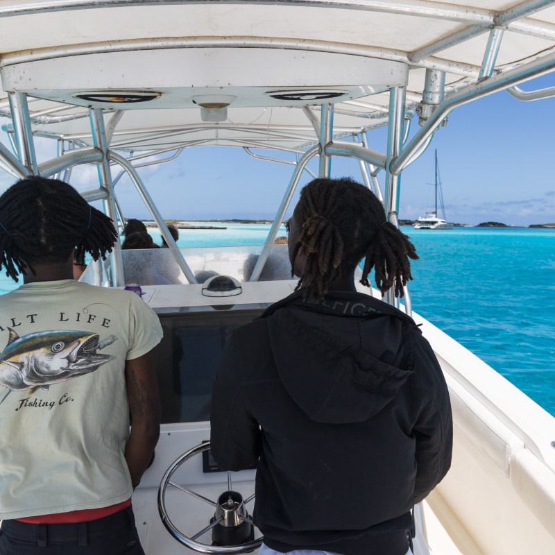Two people on a boat in clear blue water, view from behind.