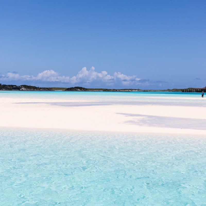 Tropical beach with white sand and clear blue water under a bright sky.