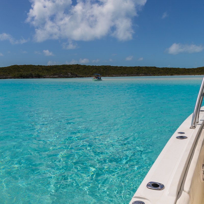Boat on clear blue tropical water near an island under a partly cloudy sky.