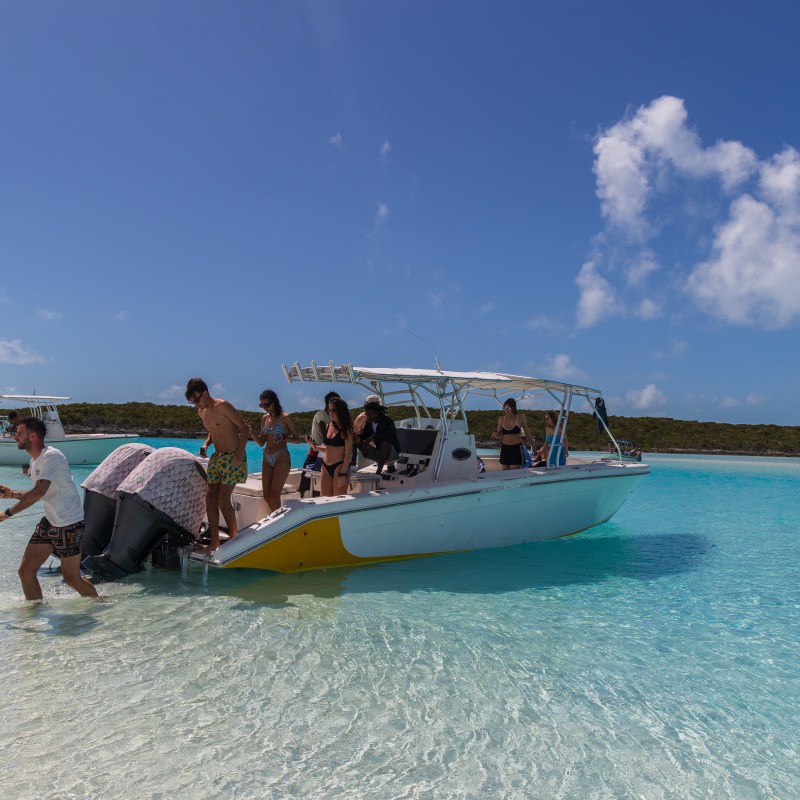Group of people on a boat in shallow, clear water with a man pulling at the front.