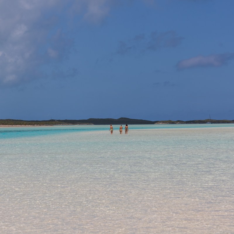 People walking in shallow turquoise water with a clear blue sky.
