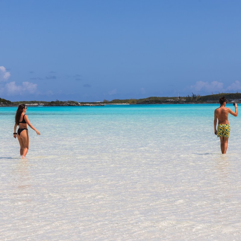 Two people walking in shallow, clear blue ocean water on a sunny day.