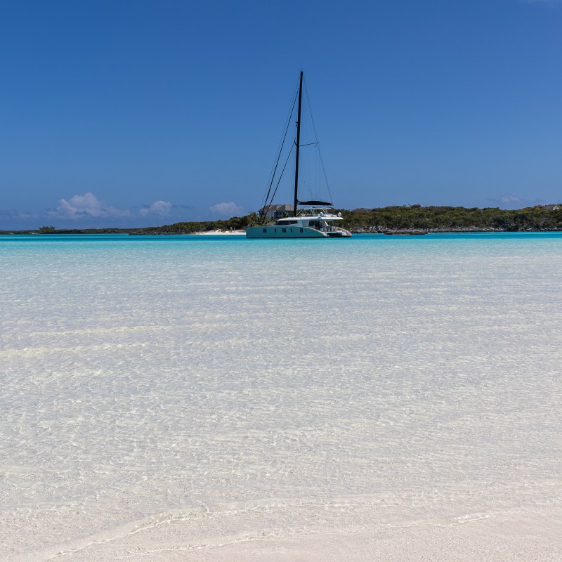 Sailboat on clear turquoise water near a sandy beach under a blue sky.