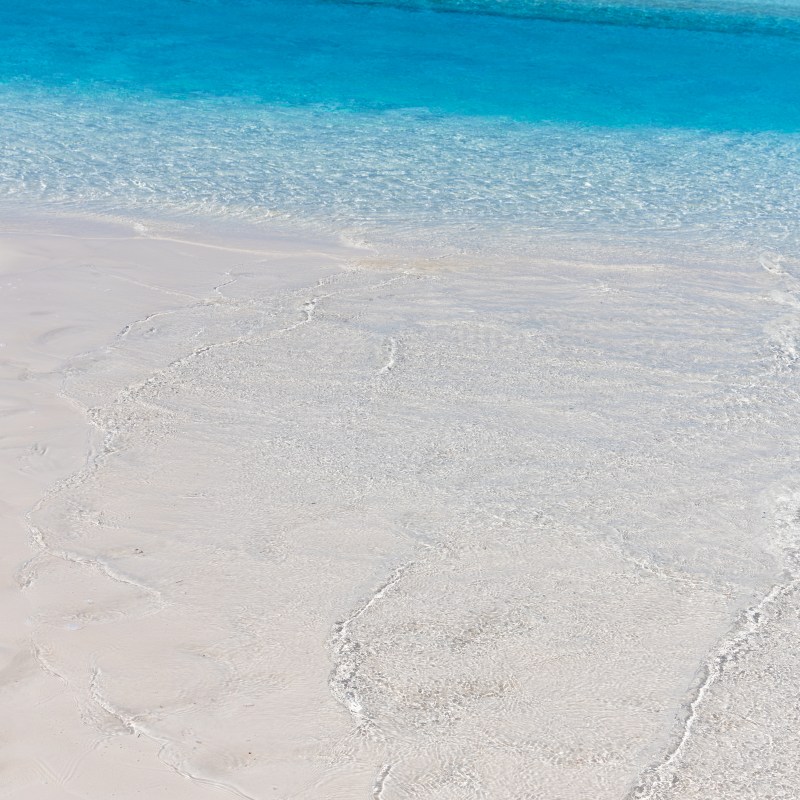 White sand beach with clear turquoise water and distant dark shoreline.