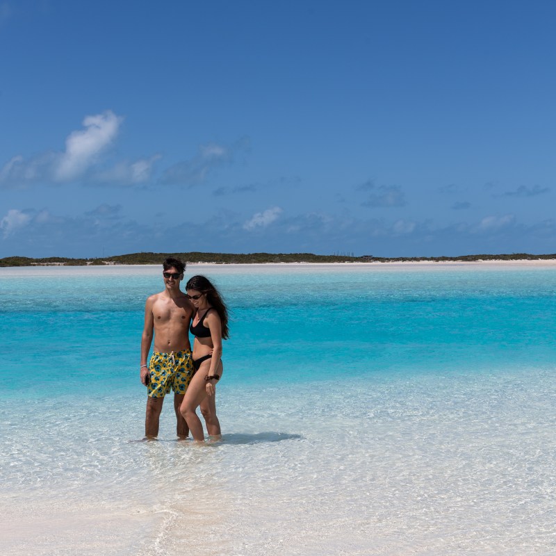 Couple standing in clear turquoise water on a sunny beach.