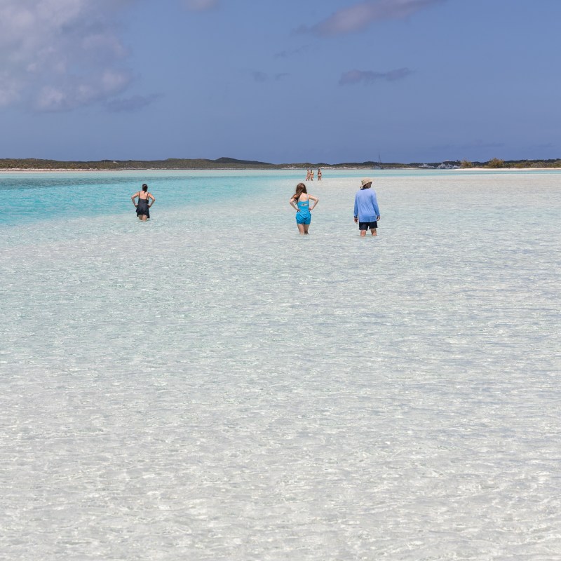 People walking in shallow, clear turquoise water under a blue sky.