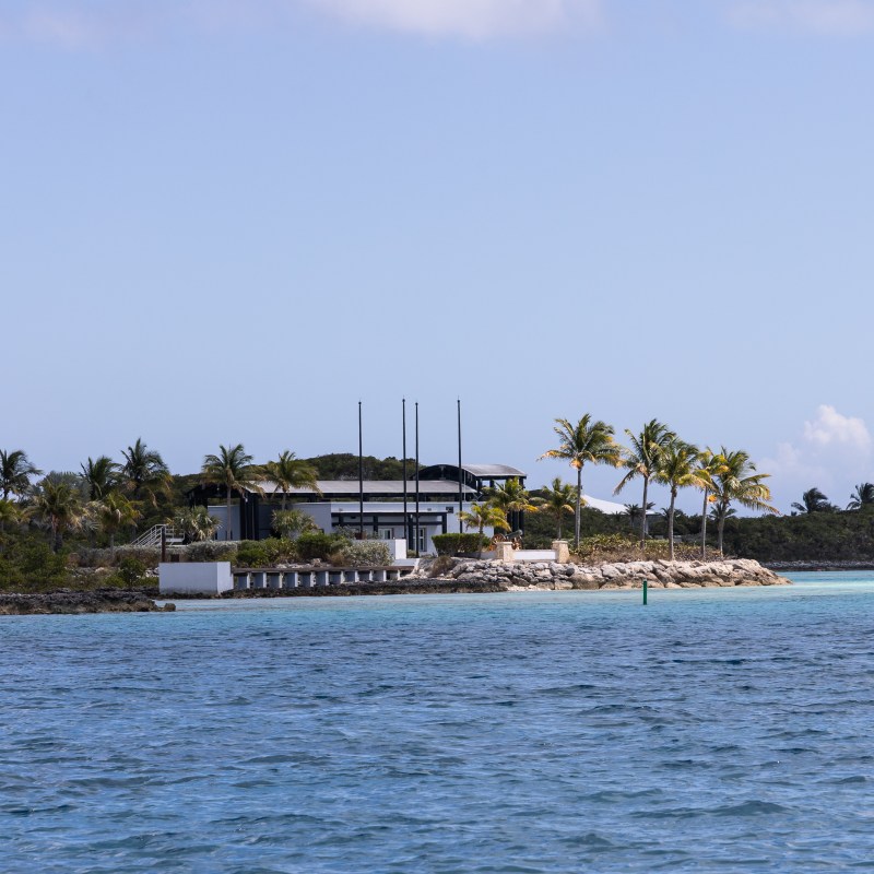 Coastal landscape with modern house, palm trees, and clear blue water.