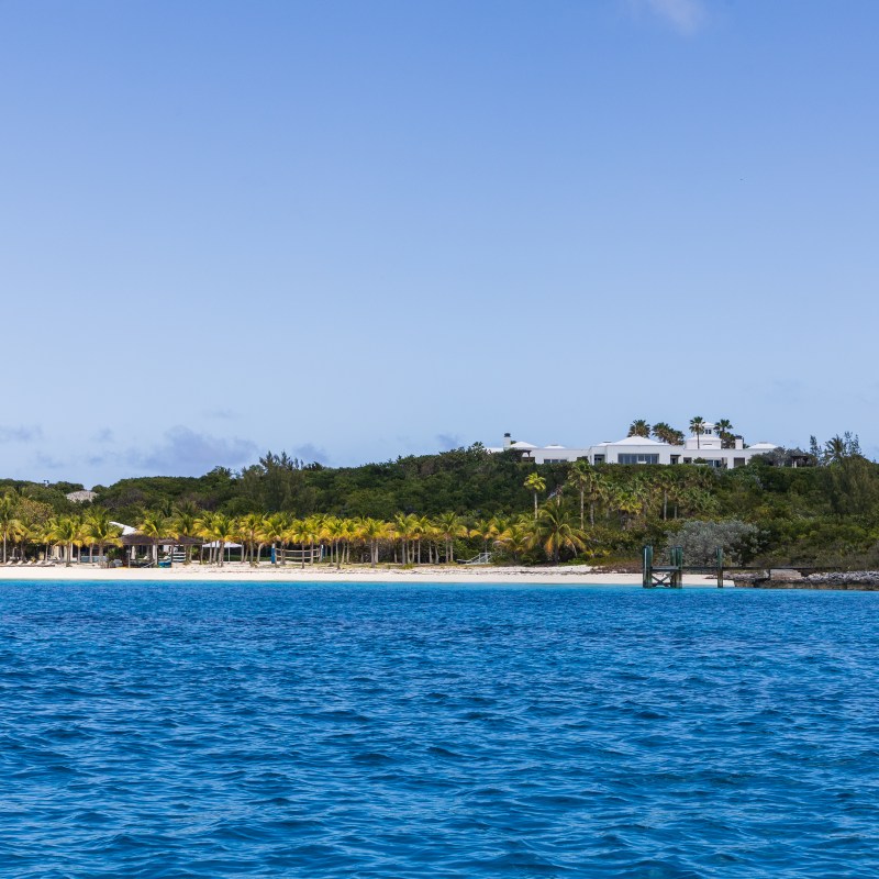 Tropical island with a beach, palm trees, and a distant building.