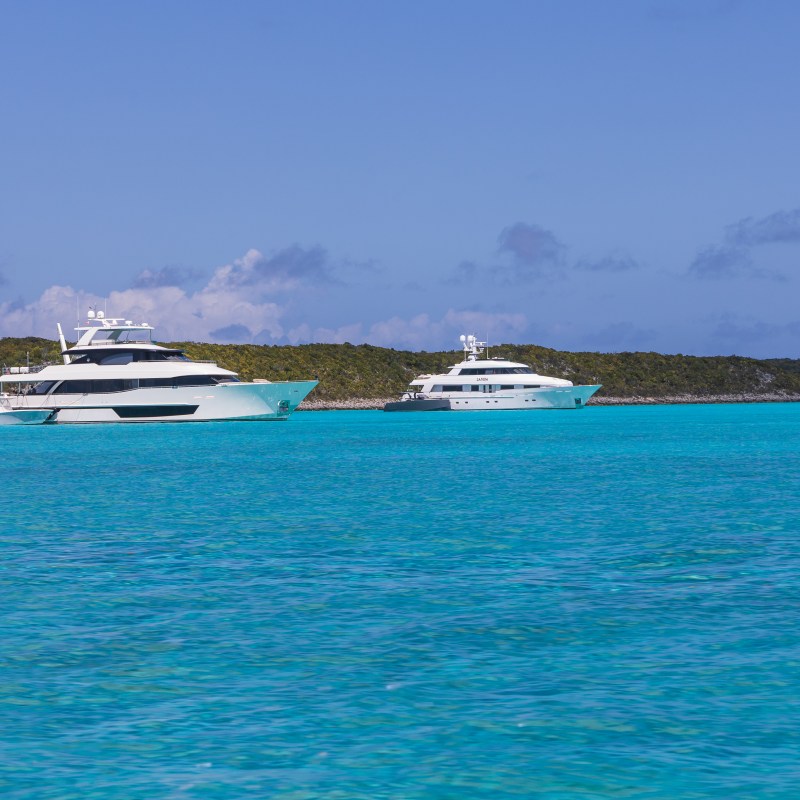 Two yachts on turquoise water with a hilly island backdrop.