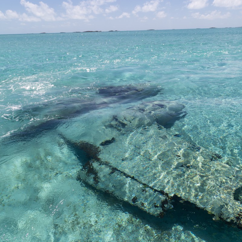 Clear ocean water with submerged rocks on a sunny day.