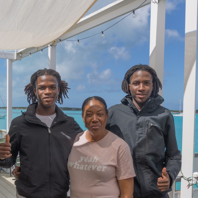 Three people smiling on a deck overlooking the ocean.