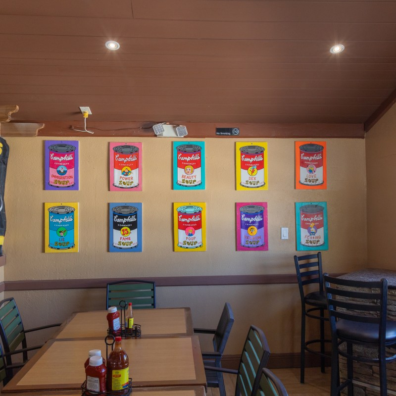 Restaurant corner with tables, chairs, and pop art soup can posters on the wall.