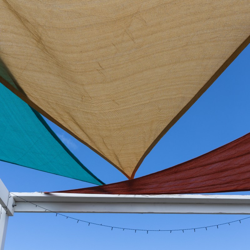 Colorful triangular fabric shades against a clear blue sky.