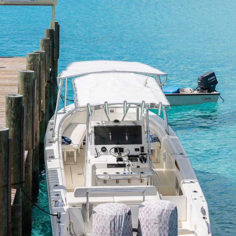 Boat docked by clear blue water, small boat in distance.