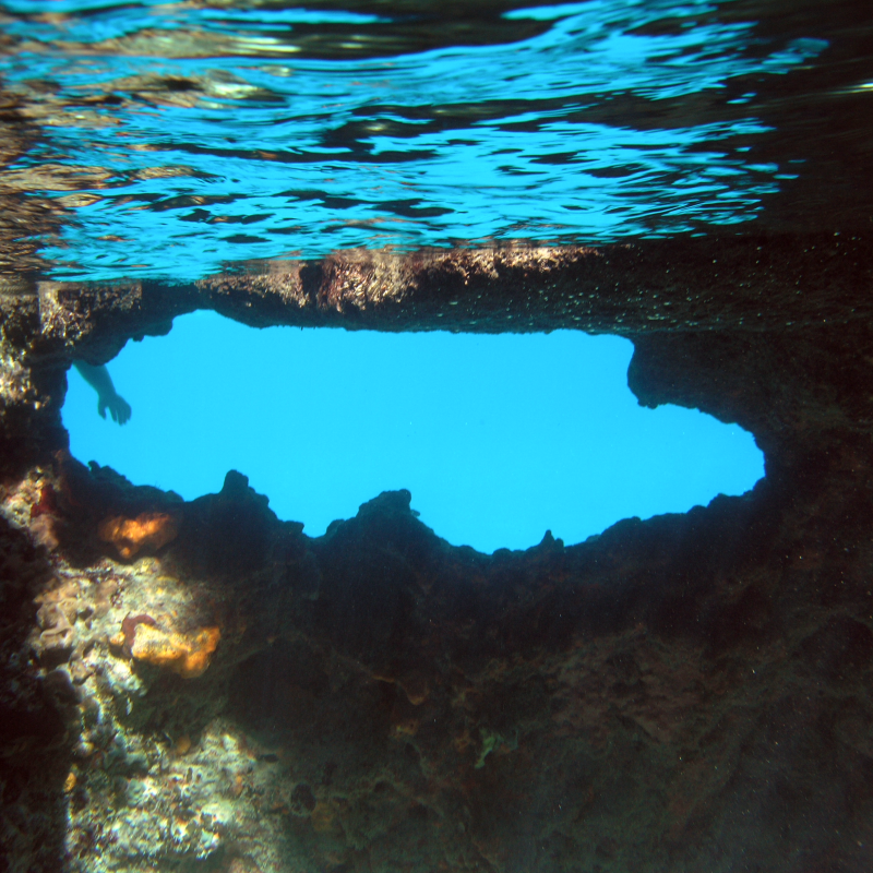 Underwater view of blue sky through a jagged rock opening.