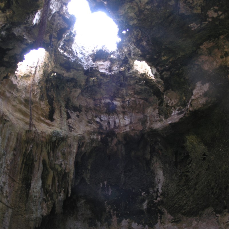 Cave interior with sunlight streaming through openings in the ceiling.