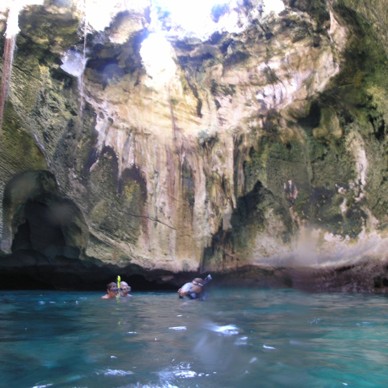 Two snorkelers in a sunlit cave with turquoise water and rocky walls.