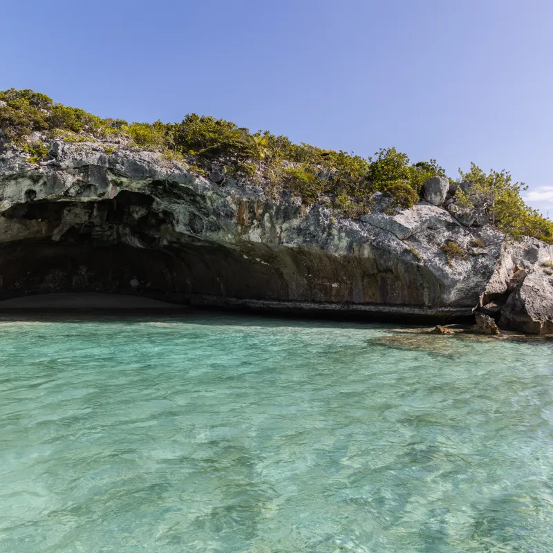 Coastal cave with clear turquoise water and rocky vegetation.